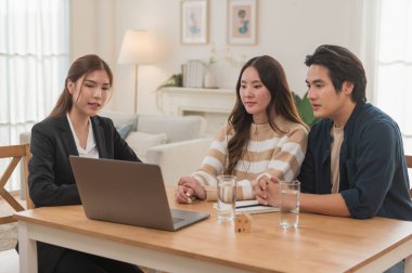 Asyalı finans danışmanı ofisteki genç çifte yeni proje yatırımını açıklıyor. Emlakçı aileyle ipotek seçeneklerini tartışıyor. Finans danışmanıyla ipotek kredisi danışmanlığı.