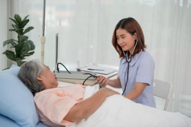 Tonometresi olan Asyalı hemşire hastanede yaşlı bir kadının tansiyonunu ölçüyor.