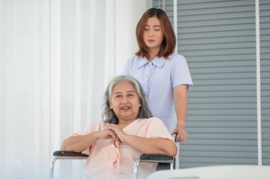Hastane koğuşunda yaşlı kadın hastayı tekerlekli sandalyeye iten Asyalı hemşire, yaşlı bakım konsepti