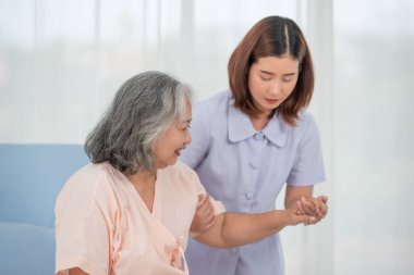 Klinikte ya da hastanede yaşlı bir kadının elini tutan gülümseyen Asyalı doktor, yaşlıların sağlık hizmetleri kavramı