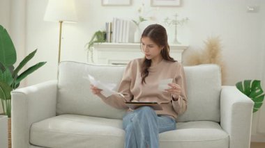 Faturaları inceleyen Asyalı kadın, mali sorunları, çek hesapları, kredi için ödeme eksikliği, büyük vergiler, kamu hizmetleri oranları, tahliye ihbarı, banka borcu tebligatı gibi sıkıntılar yaşıyor 