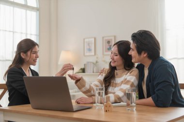 Emlakçı ev anahtarlarını müşteriye veriyor. Asyalı kadın emlakçı ev modeliyle aynı masada otururken alıcıya anahtarları veriyor. Gayrimenkul, yeni mülk alımı, ipotek konsepti