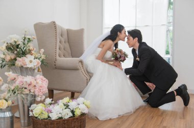 Asyalı çift evleniyor, mutlu Asyalı çift düğün kıyafetleri ve öpüşmeler, gelin beyaz bir gelinlik ve damatla klasik bir takım elbise giyiyor, ikisi de çekici ve birbirlerine aşıklar.