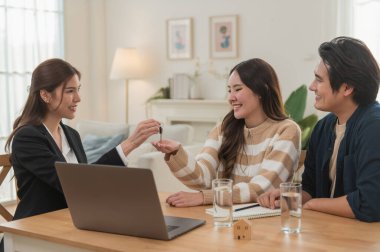 Emlakçı ev anahtarlarını müşteriye veriyor. Asyalı kadın emlakçı ev modeliyle aynı masada otururken alıcıya anahtarları veriyor. Gayrimenkul, yeni mülk alımı, ipotek konsepti