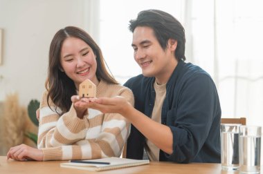 Mutlu Asyalı aile genç çiftimiz ellerinde model evlerle yeni bir ev almak için para biriktirmenin anahtarlarını gösteriyorlar. İş finansmanı, finansal planlama için banka mevduatı.