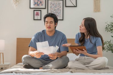 Faturaları inceleyen Asyalı çift, mali sorunlar, çek hesapları, kredi için ödeme eksikliği, büyük vergiler, kamu hizmetleri oranları, tahliye ihbarı, banka borcu tebligatı gibi sıkıntılar yaşıyor