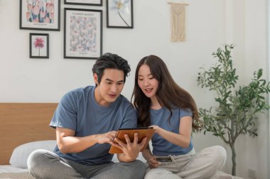 Genç Asyalı çift evde dijital tablet kullanırken online alışveriş yaparken, çift fatura ödemek için kredi kartı kullanıyor veya tatil için bir oda ayırtıyor, internette geziniyor ve online alışveriş yapıyor.