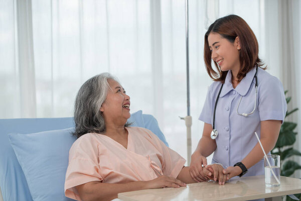 Smiling caring Asian doctor supporting holding hand of olde senior female patient at clinic or hospital, Elderly people health care concept