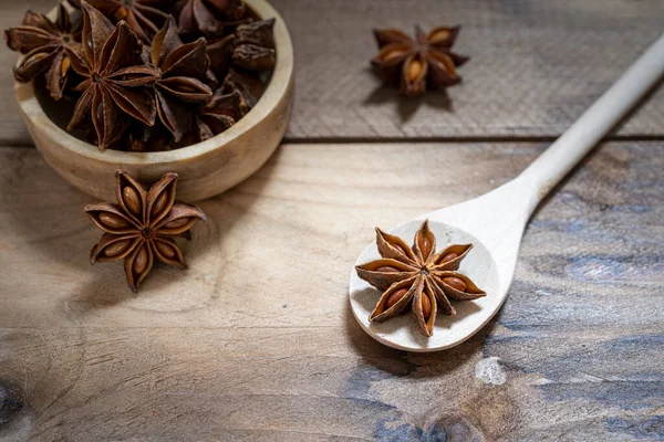 Anise stars (Illicium verum ) in wooden spoon and wooden bowl on dark rustic wooden background. Favorite spice in many food and use for medicine. Fragrant Asian spice and Herb concept.