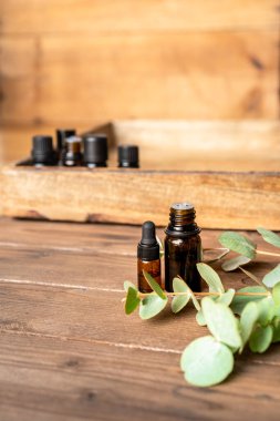 Ahşap zemin üzerinde okaliptüs dalları olan küçük cam şişelerde gerekli yağlar. Seçici odak ve metin için alanı kopyala. Doğal kozmetik ürünleri.