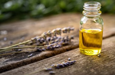 Ahşap bir masanın üzerinde lavanta filizi ve bulanık yeşil arka plan olan küçük cam bir şişedeki temel yağ. Seçici odak ve metin için alanı kopyala. Doğal kozmetik ürünleri.