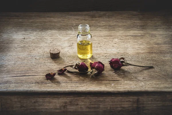 Ahşap arka planda kurumuş pembe güller olan küçük cam bir şişedeki temel yağ. Seçici odak ve metin için alanı kopyala. Doğal kozmetik ürünleri.