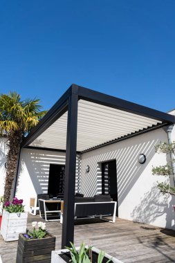 Çevre dostu biyo-mekanik alüminyum pergola gölge yapısı, tente ve teras çatısı, bahçe salonu, sandalyeler, bahçe düzeniyle çevrili metal ızgara.