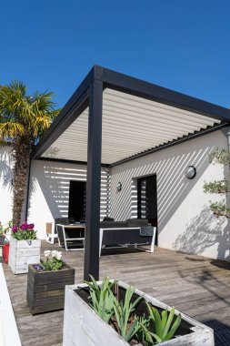 Çevre dostu biyo-mekanik alüminyum pergola gölge yapısı, tente ve teras çatısı, bahçe salonu, sandalyeler, bahçe düzeniyle çevrili metal ızgara.