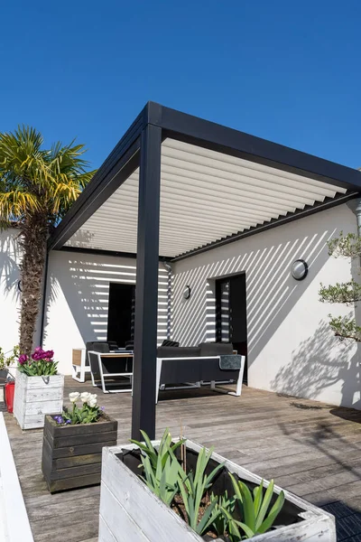 Çevre dostu biyo-mekanik alüminyum pergola gölge yapısı, tente ve teras çatısı, bahçe salonu, sandalyeler, bahçe düzeniyle çevrili metal ızgara.