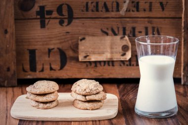 Çikolata parçalı kurabiyeler ve eski ahşap arka planda bir bardak süt.