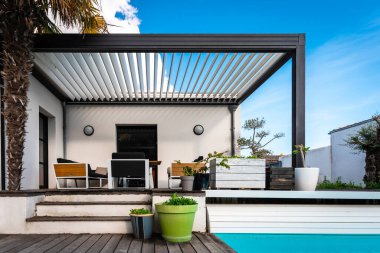 Çağdaş bir evde bahçe ve yüzme havuzuyla çevrili modern bir pergola yapısı.