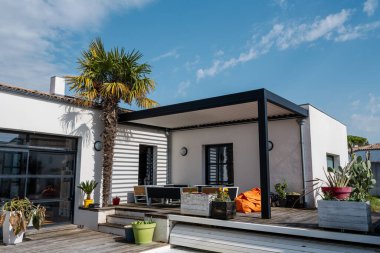 gerçekçi fotoğraf modern tasarım alüminyum levhalar ile biyolimatik pergola yüzme havuzu olan, yemek alanı bol, bitki örtüsü olan modern bir evin yanında duruyor.