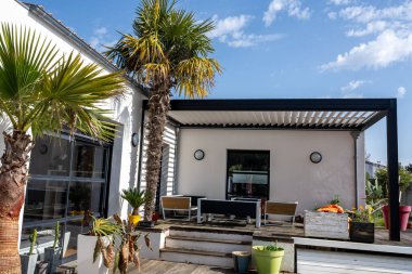 gerçekçi fotoğraf modern tasarım alüminyum levhalar ile biyolimatik pergola yüzme havuzu olan, yemek alanı bol, bitki örtüsü olan modern bir evin yanında duruyor.