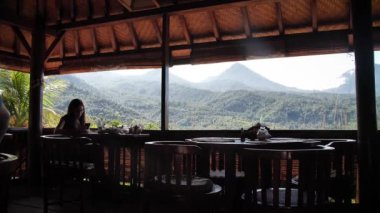 Restoran otelinde manzaralı kahvaltı yaparken telefonuna bakan bir kadın. Bali, Endonezya. Yüksek kaliteli FullHD yavaş çekim görüntüleri.