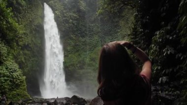 Ormanın ortasında Nungnung Şelalesi 'ni fotoğraflayan kadın. Bali, Endonezya. Yüksek kaliteli FullHD yavaş çekim görüntüleri.