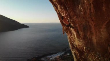 Günbatımında Grande Grotta mağarasının sert ve dik bir bölümüne tırmanan dağcı ve Yunanistan 'ın Kalymnos adasının arkasındaki Telendos adası ve kıyı şeridi. Yüksek kalite 4k görüntü.