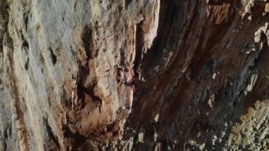 Günbatımında Grande Grotta mağarasının sert ve dik bir bölümüne tırmanan dağcı ve Yunanistan 'ın Kalymnos adasının arkasındaki Telendos adası ve kıyı şeridi. Yüksek kalite 4k görüntü.