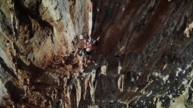 Günbatımında Grande Grotta mağarasının sert ve dik bir bölümüne tırmanan dağcı ve Yunanistan 'ın Kalymnos adasının arkasındaki Telendos adası ve kıyı şeridi. Yüksek kalite 4k görüntü.