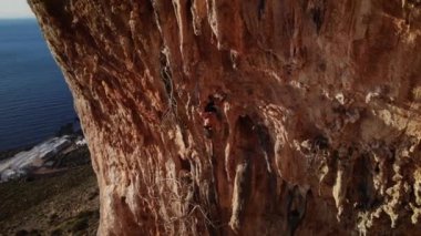 Günbatımında Grande Grotta mağarasının sert ve dik bir bölümüne tırmanan dağcı ve Yunanistan 'ın Kalymnos adasının arkasındaki Telendos adası ve kıyı şeridi. Yüksek kalite 4k görüntü.