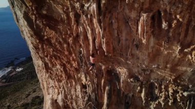 Günbatımında Grande Grotta Mağarası 'nın sert ve dik bir bölümünde ve Yunanistan' ın Kalymnos adasının arkasındaki Telendos adasında dinlenmeye çalışan dağcı. Yüksek kalite 4k görüntü.