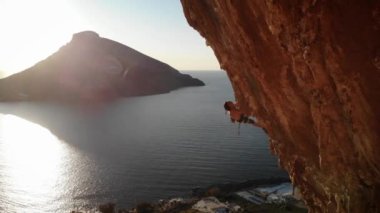 Günbatımında Grande Grotta Mağarası 'nın sert ve dik bir bölümünde ve Yunanistan' ın Kalymnos adasının arkasındaki Telendos adasında dinlenmeye çalışan dağcı. Yüksek kalite 4k görüntü.