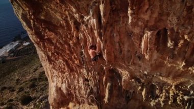 Günbatımında Grande Grotta Mağarası 'nın sert ve dik bir bölümünde ve Yunanistan' ın Kalymnos adasının arkasındaki Telendos adasında dinlenmeye çalışan dağcı. Yüksek kalite 4k görüntü.