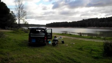 İspanya Valencia 'da bir yerlerde nefes kesici göl ve orman manzaralı bir karavanda kahvaltı yapan bir kadının 4K görüntüsü. Yüksek kalite 4k görüntü