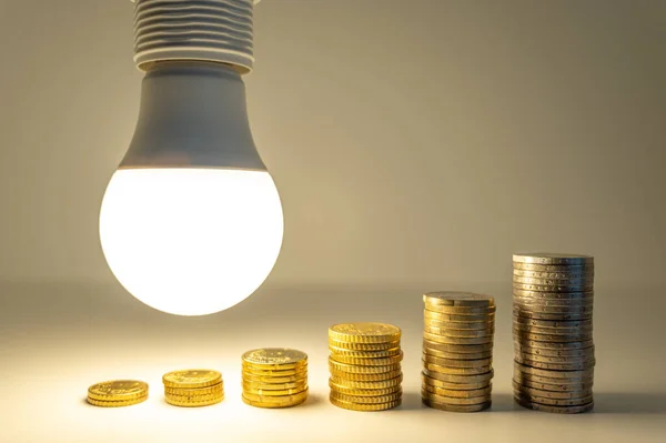 Stock image Lit light bulb with coins beside it. Increase in energy tariffs. Efficiency and energy saving. 