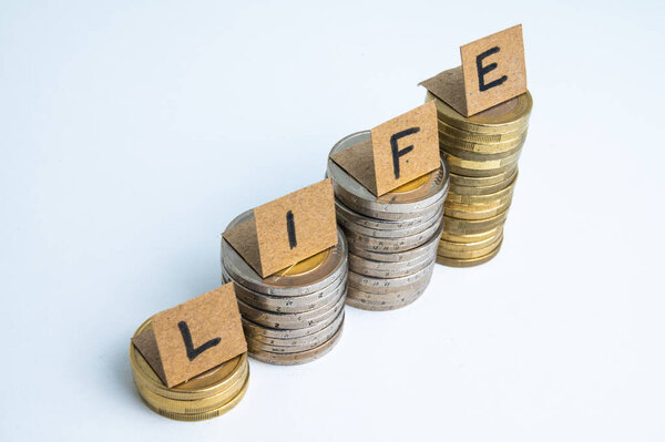 Stacks of coins, and above tickets spelling the word "life". Rising cost of living. Increase in earnings.