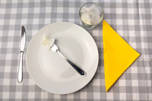 Laid table, with white plates and glass containing plastic waste. Plastic in the environment and microplastics in food.