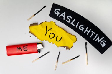 Word Gaslighting, on a black surface, next to a lighter with the word Me, and burnt yellow card with the writing You. Psychological meaning. clipart