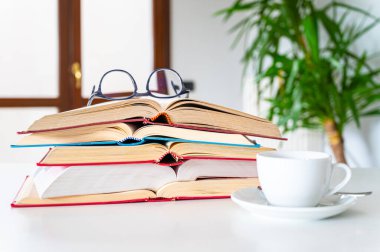 Masada yığınla kitap, yanında bardak ve bardakla. Çalış ve kültür.