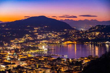 The city of Como, photographed in the evening, with the lakefront, the cathedral, and the surrounding mountains.