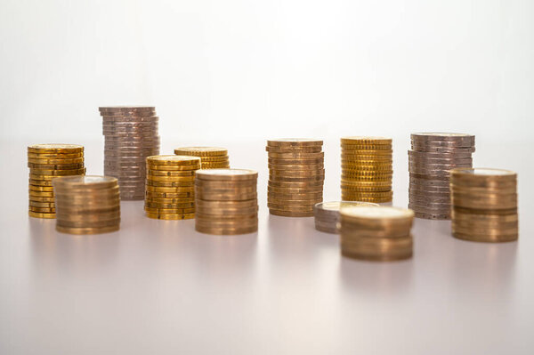 Stacks of coins next to each other, on white surface. Quantity of money, currency and wealth.