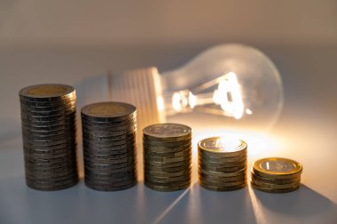 Yükselen bozuk para yığınlarıyla aydınlık lamba. Enerji tarifelerinde azalma.