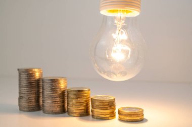 Yükselen bozuk para yığınlarıyla aydınlık lamba. Enerji tarifelerinde azalma.