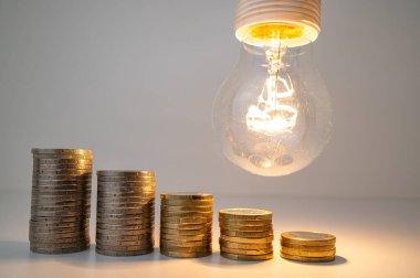 Yükselen bozuk para yığınlarıyla aydınlık lamba. Enerji tarifelerinde azalma.