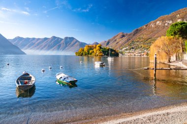 Comacina Adası, sonbaharda ağaçlarla, teknelerle ve rıhtımlarla çekilmiş..