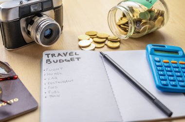 Seyahat bütçesi ve harcama listesi olan bir defter. Yanında da kamera, gözlük, para, hesap makinesi. Seyahat masrafları.