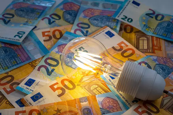 Light bulb lit, above euro banknotes. Electricity cost and tariffs.