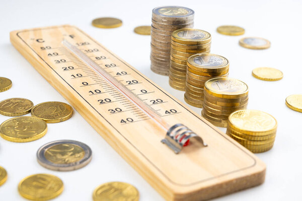 Room thermometer and stacks of coins and money. Space heating costs.