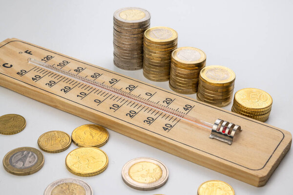 Room thermometer and stacks of coins and money. Space heating costs.