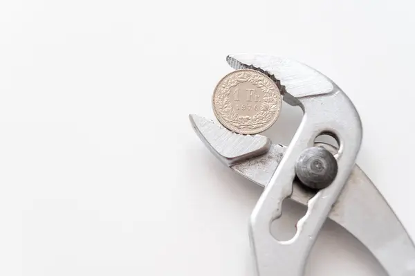 Stock image Pliers holding Swiss Franc coin. Financial pressures and squeezes on the currency.