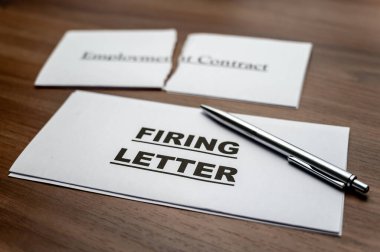 Torn employment contract, and next to it a firing letter, on a wooden surface. clipart